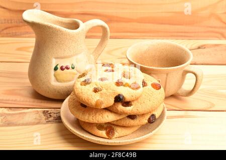 Mehrere runde duftende, frisch, lecker, süß, Kekse mit Rosinen, In einer Keramikuntertasse und mit Keramikbecher und Milchkännchen, Nahaufnahme. Stockfoto