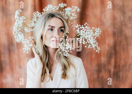 Nahaufnahme der charmanten glücklichen Frau in Frühlingsstimmung mit Gypsophila-Blumen auf ihrem Kopf. Lifestyle-Porträt einer selbstbewussten Frau in den Dreißigern. Stockfoto