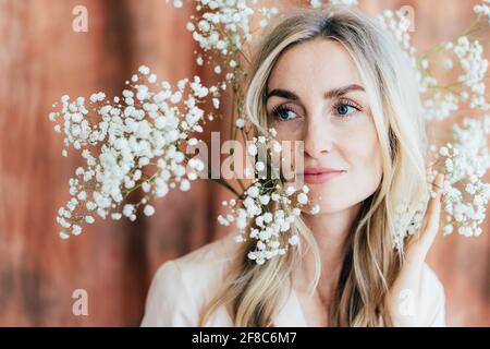 Nahaufnahme der charmanten glücklichen Frau in Frühlingsstimmung mit Gypsophila-Blumen auf ihrem Kopf. Lifestyle-Porträt einer selbstbewussten Frau in den Dreißigern. Stockfoto