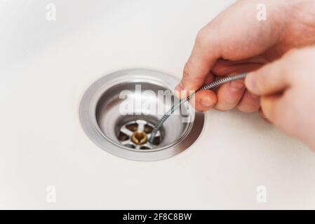 Klempner, der Abflussschlange verwendet, um das Spülbecken der Küche zu entverstopfen. Stockfoto