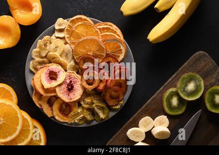 Getrocknete, geschnittene Pflaumen, Kiwi, Pfirsich-Früchte-Chips in Form eines Herztellers auf schwarzem Hintergrund, Heimtrocknung. Snack vegan frei von Zucker. Blick von oben. Stockfoto