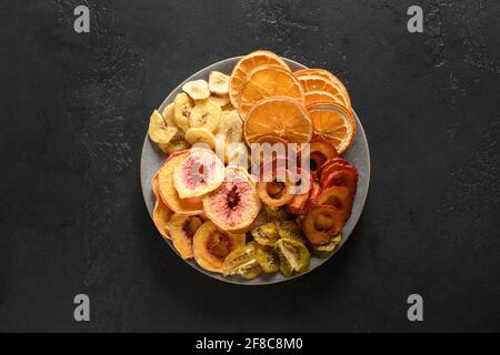 Früchte Pflaumen, Kiwi, Pfirsich Früchte Chips auf schwarzem Hintergrund, Heimtrocknung. Snack vegan frei von Zucker. Blick von oben. Stockfoto