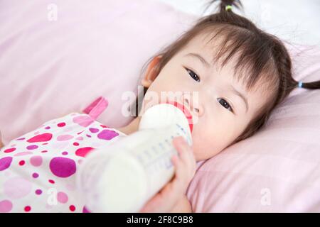 Schöne kleine asiatische Mädchen liegen und saugen Milchflasche Im Bett Stockfoto