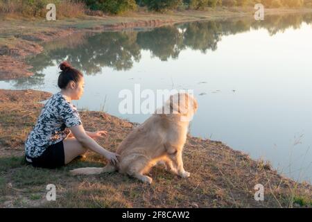 Frau und Golden Retriever Hund sitzen in der Nähe von Fluss oder See Stockfoto