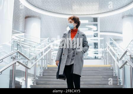Junge Frau in einer Schutzmaske, die in der U-Bahn die Treppe hinunter geht. Stockfoto