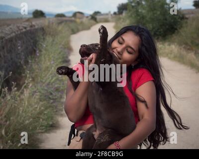 Asiatischer Teenager, der mit einem drei Monate alten Schokoladenretriever-Welpe auf einem Feldweg auf dem Land spielt. Stockfoto