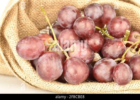 Ein Bund frischer, saftiger, reifer, süßer Trauben aus biologischem Anbau in einem Jutebeutel, aus nächster Nähe, auf weißem Hintergrund. Stockfoto