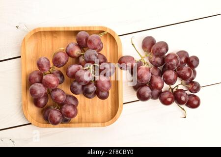 Zwei Trauben frischer organischer, saftiger, reifer, süßer Trauben mit einem Bambustablett, aus nächster Nähe, auf einem bemalten Tisch aus Holz. Stockfoto