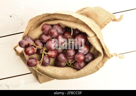Ein Bund frischer organischer, saftiger, reifer, süßer Trauben in einem Jutebeutel, Makro, auf einem bemalten Tisch aus Holz. Stockfoto