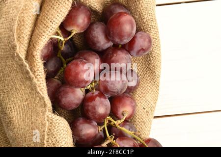 Ein Bund frischer organischer, saftiger, reifer, süßer Trauben in einem Jutebeutel, Makro, auf einem bemalten Tisch aus Holz. Stockfoto