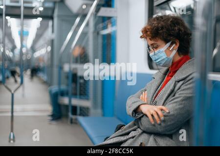 Müde Frau in einer Schutzmaske schläft in einem leeren U-Bahn-Auto. Stockfoto