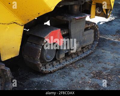 Fragment eines Bulldozers mit Raupenrad auf einer übersäten, unbefestigten Straße. Caterpillar auf einem Asphaltfertiger. Stockfoto