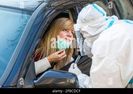 Medizinisches Personal Durchführen Drive-Thru COVID-19 Test, unter nasalen Tupfer Probe von weiblichen Patienten durch Auto-Fenster, PCR-Diagnose für Coronavirus, d Stockfoto