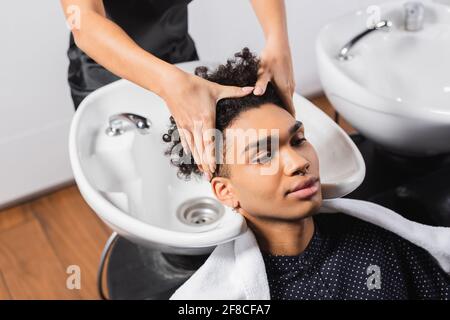 Afroamerikanischer Mann, der in der Nähe des Friseurs sitzt und Haare und Waschbecken wäscht Auf unscharfem Hintergrund Stockfoto