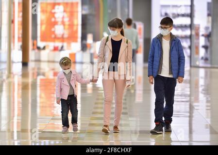 Mama und Kinder mit Gesichtsmasken gehen durch den Einkauf Zentrum während der COVID-19-Pandemie Stockfoto