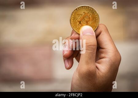Nahaufnahme einer goldenen Münze mit dem Bitcoin-Symbol in der Hand. Junge Hand hält Kryptowährung Münze, Geld Münzen digital, BTC Stockfoto