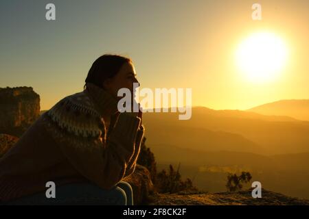 Hintergrundbeleuchtetes Profil einer Frau, die bei Sonnenuntergang meditiert Der Berg Stockfoto