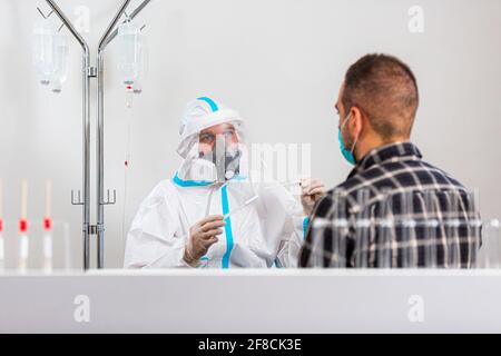 Medizinisches Personal, das COVID-19 Test durchführt, nasale Abstrichprobe vom männlichen Patienten im Krankenhauslabor nimmt, PCR-Diagnostik für Coronavirus, Doktor in PPE usi Stockfoto