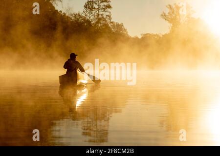 Kanufahrt bei Sonnenaufgang auf einem nebligen Fluss. Stockfoto