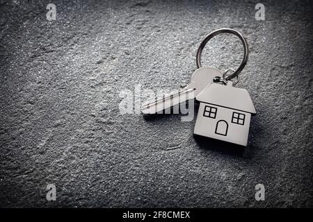 Hausschlüssel auf einem hausförmigen Schlüsselanhänger auf Stein Konzept für Immobilien, Umzug nach Hause oder Vermietung von Immobilien Stockfoto