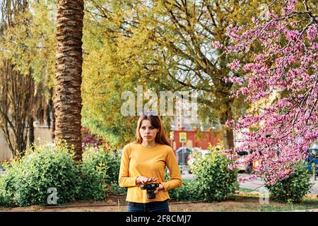 Junges Mädchen, das mit einer Fotokamera im Park spazieren geht Im Frühling Stockfoto