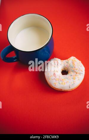 Gebissen Donut in Glasur und blaue Tasse Milch auf Roter Hintergrund Stockfoto