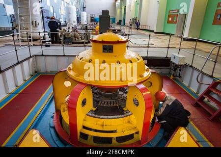 Maschinenraum des Wasserkraftwerks Shardara. Gelbe Generatormaschine und Arbeiter. Kasachstan. Stockfoto