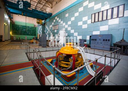 Maschinenraum des Wasserkraftwerks Shardara. Gelbe Generatormaschine und blauer Kran. Altmodisches sowjetisches Interieur. Kasachstan. Stockfoto