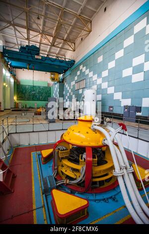 Maschinenraum des Wasserkraftwerks Shardara. Gelbe Generatormaschine und blauer Kran. Altmodisches sowjetisches Interieur. Kasachstan. Stockfoto