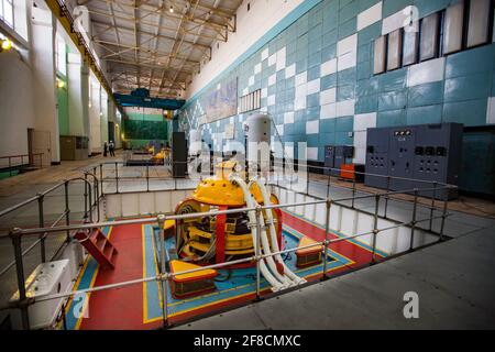 Maschinenraum des Wasserkraftwerks Shardara. Gelbe Generatormaschine und blauer Kran. Altmodisches sowjetisches Interieur. Kasachstan. Stockfoto