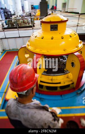 Maschinenraum des Wasserkraftwerks Shardara. Gelbe Generatormaschine und Arbeiter. Tilt-Shift – teilweise verschwommener Effekt. Geringe Schärfentiefe. Kasachstan Stockfoto