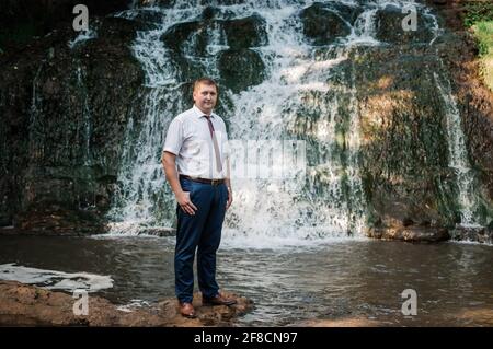Ein Mann steht vor dem Hintergrund eines Wasserfalls Stockfoto