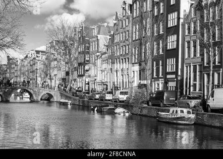 Amsterdam, Niederlande - 24. Februar 2017: Schwarz-weiß Blick auf den Amsterdamer Kanal, gewöhnliche Menschen laufen an der Küste in der Nähe alter Wohnhäuser Stockfoto