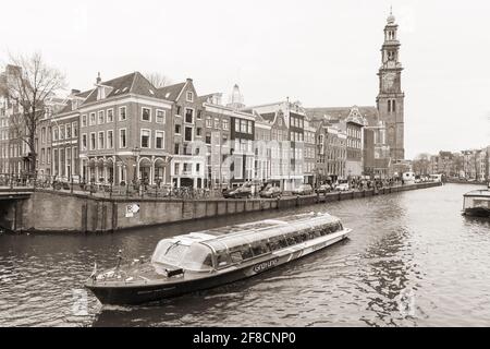 Amsterdam, Niederlande - 25. Februar 2017: Sepiafarbtes Foto mit Touristenboot auf dem Amsterdamer Kanal und Westerkerk Turm auf einem Hintergrund Stockfoto