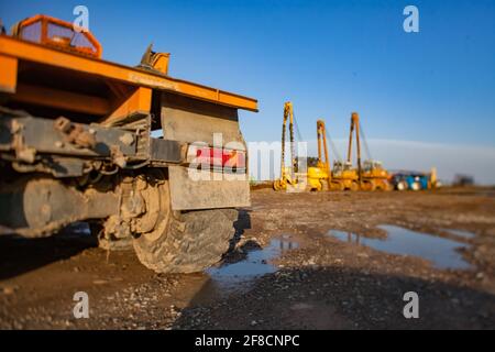 Gelbe Bau-Raupenmaschinen auf dem Parkplatz (rechts). Neigungsverschobenes, teilweise verschwommenes Foto. Turkestan, Kasachstan. Stockfoto