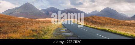 Weite Panorama-Berglandschaft mit leerer, gepflasterter Straße, die sich zu den Red Cuillin Hills bei Sligachan auf der Isle of Skye, Schottland, schlängelt. Stockfoto