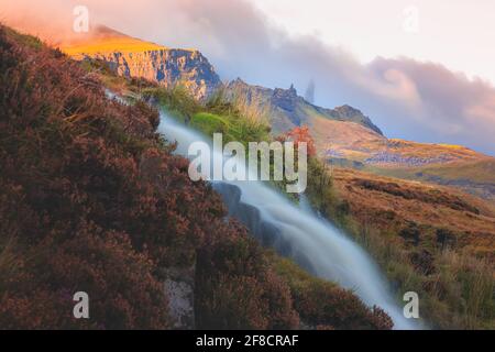 Goldenes Licht und lebhafter, farbenfroher Sonnenuntergang- oder Sonnenaufgangshimmel über der dramatischen Landschaft des Old man of Storr mit dem Wasserfall Bride's Veil Falls auf der Isle of Stockfoto