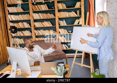 Glückliche, schöne Geschäftsfrau, die dem Chef eine Präsentation macht, über Arbeitsberichte spricht, lächelt. afroamerikanischer männlicher Mitarbeiter genehmigte die Projektidee Stockfoto