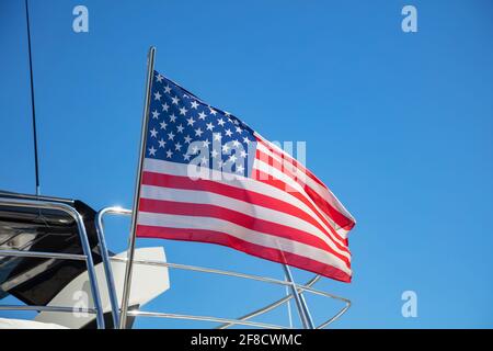 Flagge der Vereinigten Staaten von Amerika winkt auf dem Heck der Yacht. Luxusboot, das an der Marina in Athen, Griechenland, festgemacht ist. Blauer Himmel, Nahaufnahme. Stockfoto