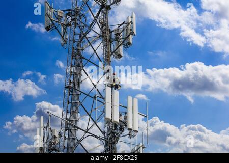 Wartung der Telekommunikation. Mann Kletterer auf Turm gegen blau bewölkten Himmel Hintergrund. Telekommunikation Maststation, TV-Antenne drahtlose Technologie Stockfoto