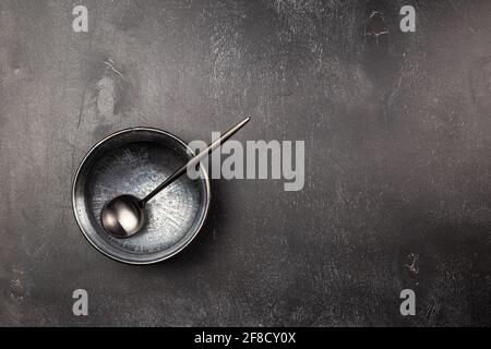 Leerer schwarzer Tonschüsselteller und schwarzer Metalllöffel auf Holztisch. Monochromatische Farben Stockfoto