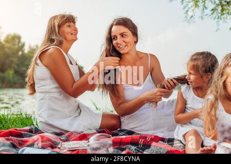 Muttertag. Mutter, Großmutter und Tochter weben sich Haarflechten. Familie, die Spaß beim Frühjahrspicknick im Park hat. Stockfoto