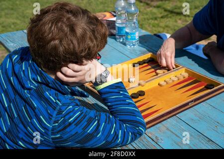 Ein Junge und eine Frau spielen an einem sonnigen Tag Backgammon im Freien. Stockfoto