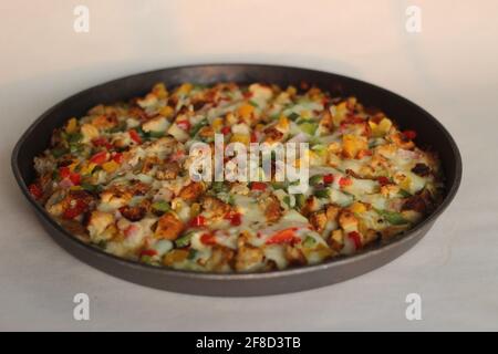 Eine hausgemachte Pizza mit dünner Kruste, die mit Käse, Huhn und Gemüse beladen ist. Aufgenommen auf weißem Hintergrund. Stockfoto