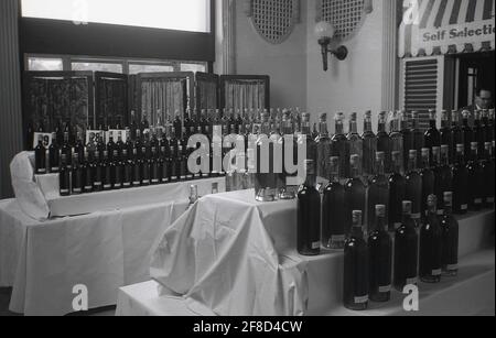 1963, in einer Halle, Flaschen Wein auf einer Amateur-Winzer-Messe, England, Großbritannien, ausgestellt. In dieser Zeit waren die häusliche Weinherstellung und das Bierbrauen beliebte Hobbys, und es wurden Messen mit Präsentationen und Vorträgen abgehalten. Winzer bildeten Clubs und stellten ihre Produkte aus, um von ihren Kollegen beurteilt zu werden. Die Weinvereine waren als Weinkreise bekannt. Die National Association of Wine and Beermakers (NAWB), eine Amateurorganisation, wurde gegründet und fand 1959 ihren ersten Kongress in Andover statt. Die Weine wurden aus verschiedenen Zutaten hergestellt: Holunderblüte, Walnussblatt, Pastinak, Traube, Orange, Petersilie, Brennnessel und Erdbeere. Stockfoto