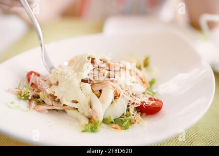 Gabel in weißem Teller mit Salat. Mittagsmenü. Salat mit Eiern, Salat, Kirschtomaten, Hühnchen und Käse. Gesunde Ernährung. Stockfoto