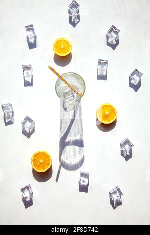 Ein leeres Glas mit einem großen Schatten, Eiswürfeln und orangefarbenen Scheiben auf weißem Hintergrund. Solarfotografie. Blick von oben, heißer Sommer und Getränk Conce Stockfoto