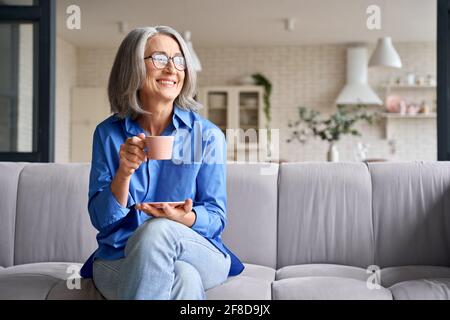 Ältere lächelnde 60s Frau Porträt zu Hause Blick weg mit einer Tasse Tee, Kaffee. Stockfoto