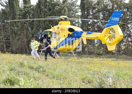 Limoux Aude France 04.13.21 zwei Sanitäter laufen von ihrem Hubschrauber aus, der auf einem Feld geparkt ist. Leuchtend gelbe Ambulanz mit blauem Streifen. Feld mit Bäumen Stockfoto