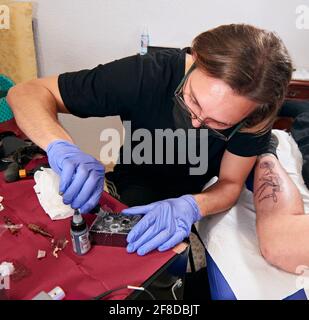 Tätowierer in blauen Handschuhen, die ein Tattoo auf dem machen Bein eines Mannes in einem Studio Stockfoto